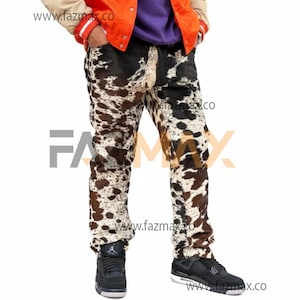 Puede incluir: Pantalones vaqueros con estampado de piel de vaca, con manchas negras, marrones y blancas. Los vaqueros se llevan con zapatillas negras. La imagen también muestra una chaqueta y la dirección del sitio web www.fazmax.co.