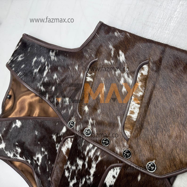 May include: A close-up of a brown and white cowhide vest with a brown leather trim. The vest has decorative silver buttons and a satin lining. The website www.fazmax.co is visible in the image.