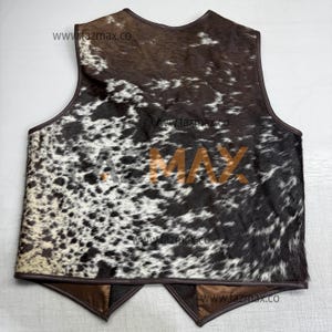 May include: A cowhide vest with a brown leather trim. The vest features a spotted pattern in shades of brown, black, and white. The text "FAZ MAX" is printed in the center of the vest. The website address "www.fazmax.co" is printed multiple times.
