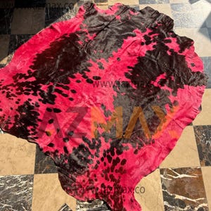 May include: A cowhide rug featuring a striking pink and black spotted design. The rug has a natural form and texture, with the website address "www.fazmax.co" printed on it. This decorative rug adds a bold statement to any room.