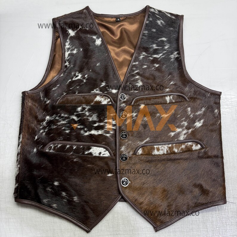 May include: A brown and white cowhide vest with a V-neck and four front pockets. The vest has a brown leather trim and four decorative buttons down the front. The interior lining is a light brown color.