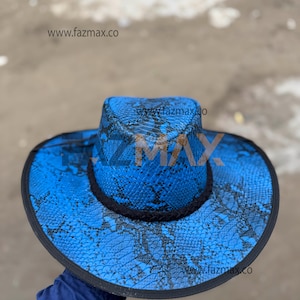 Pode incluir: Um chapéu de cowboy azul com um padrão de pele de cobra. O chapéu tem uma borda preta ao redor da aba e da coroa. O texto "www.fazmax.co" é visível no chapéu.