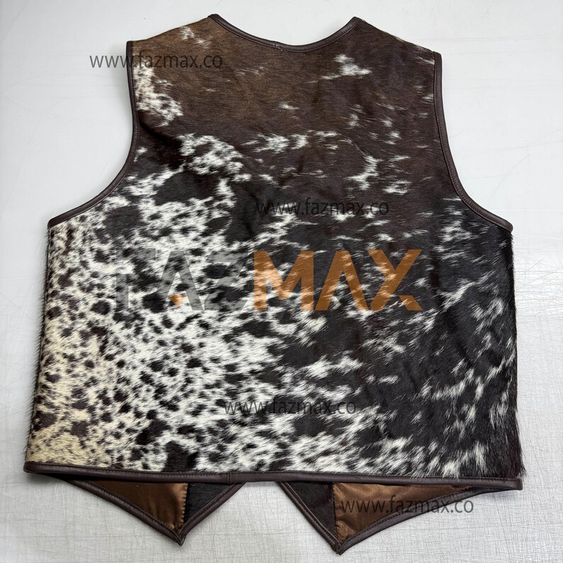 May include: A cowhide vest with a brown leather trim. The vest features a spotted pattern of black and white, with brown accents. The text "FAZ MAX" is printed in the center of the vest. The website address "www.fazmax.co" is printed multiple times.