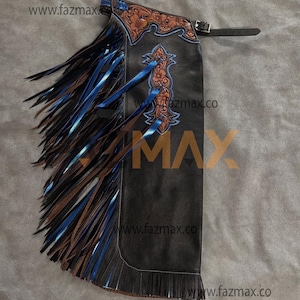 May include: Black leather chaps with brown and blue fringe and decorative tooling. The chaps feature a belt closure and are embellished with blue ribbons and floral patterns. The www.fazmax.co website is visible.