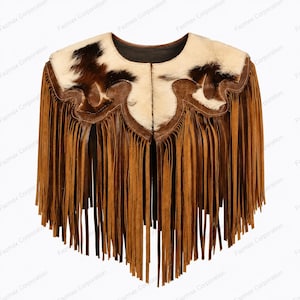 Op de afbeelding: Een bruine suède cape met lange franjes langs de onderrand. Het bovenste gedeelte is geaccentueerd met een wit en donkerbruin koeienhuidpatroon, voorzien van een geschulpte leren rand die de huid scheidt van de franjes.