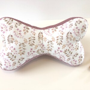 May include: A bone-shaped pillow with a white background and a floral pattern in shades of brown and pink. The pillow has a pink border.
