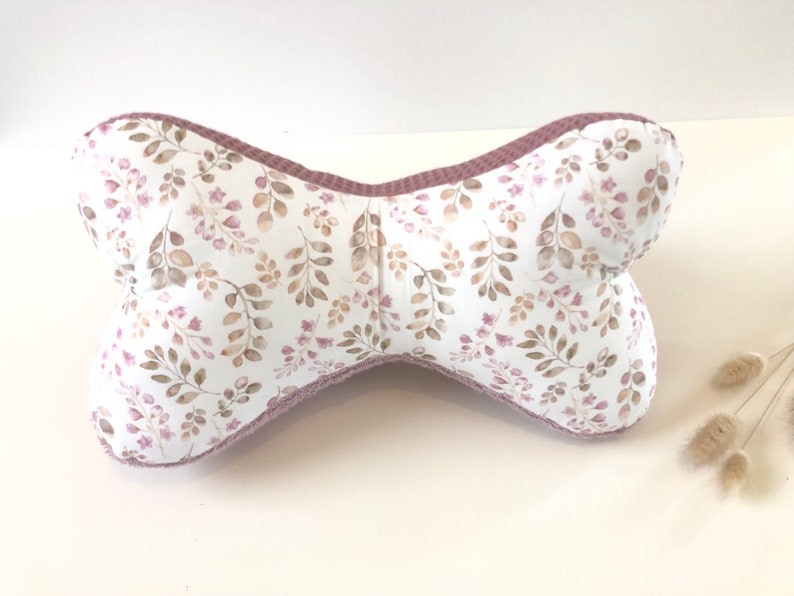 May include: A bone-shaped pillow with a white background and a floral pattern in shades of brown and pink. The pillow has a pink border.