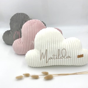 Könnte beinhalten: Drei plüschige Wolkenkissen in Grau, Rosa und Weiß mit gestickten Namen. Das weiße Kissen hat den Namen "Matilda" gestickt.