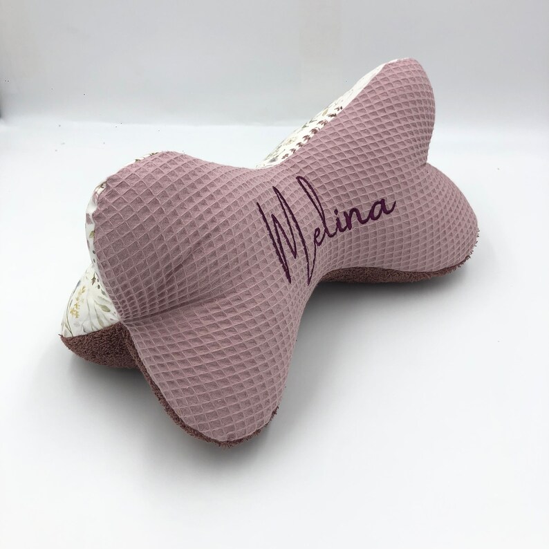 May include: A pink and white waffle-textured pillow with the name "Melina" embroidered in purple.