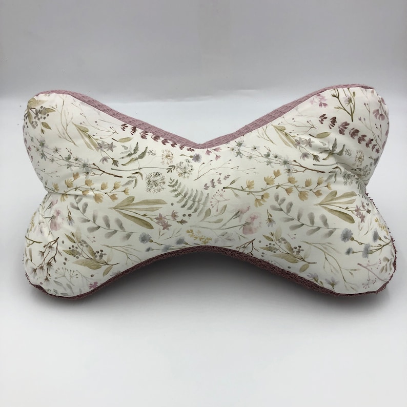 May include: A pink and white floral patterned pillow with a unique bowtie shape. The pillow is made of soft fabric and has a subtle sheen.