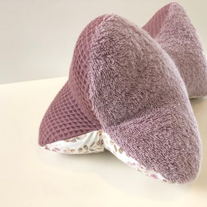 May include: A mauve-colored pillow with a waffle texture on one side and a soft, fuzzy texture on the other side. The pillow is filled with a white fabric with a floral pattern.