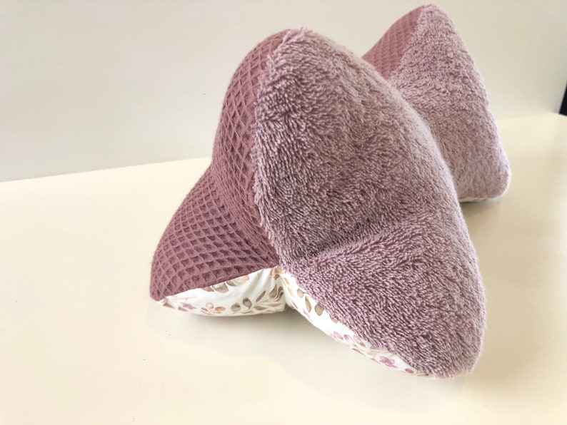 May include: A mauve-colored pillow with a waffle texture on one side and a soft, fuzzy texture on the other side. The pillow is filled with a white fabric with a floral pattern.