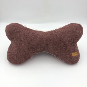 May include: A brown plush dog bone shaped pillow with a white and floral patterned fabric on the back. The pillow has a small brown label with the word "Tubby" on it.