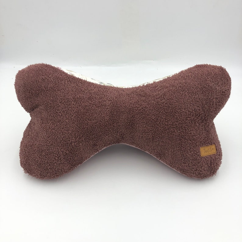 May include: A brown plush dog bone shaped pillow with a white and floral patterned fabric on the back. The pillow has a small brown label with the word "Tubby" on it.