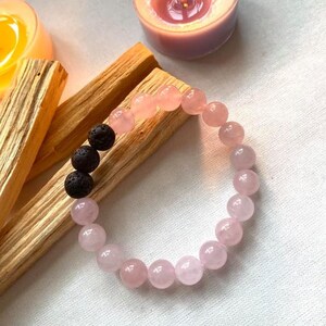 Puede incluir: Un brazalete de cuentas rosa y negro con una fila de cuentas de lava negra y una fila de cuentas de cuarzo rosa.