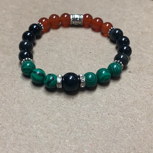 Peut inclure: Un bracelet composé de perles de cornaline, d'onyx noir et de malachite. Le bracelet a une perle d'espacement argentée avec un motif décoratif.