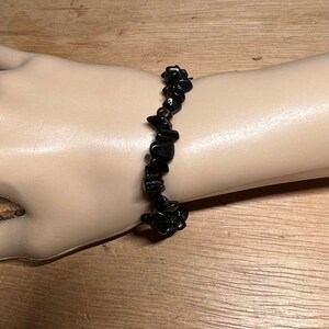 May include: Black gemstone chip bracelet. The bracelet is made of small, irregular black stones strung together on a clear elastic cord.