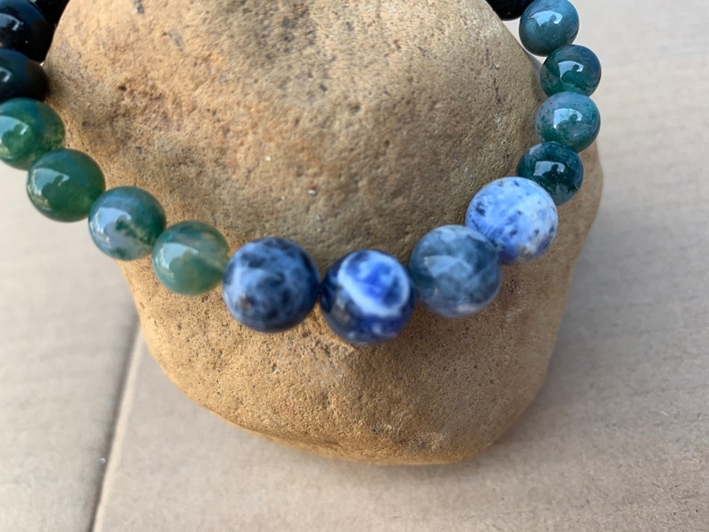 Puede incluir: Un brazalete de cuentas con piedras verdes y azules. El brazalete est&aacute; hecho de cuentas redondas con un degradado de verde a azul.