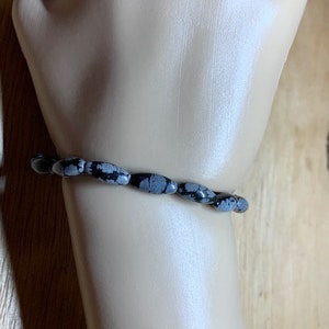 Puede incluir: Un brazalete de piedra moteada en blanco y negro con cuentas ovaladas.