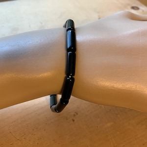 Puede incluir: Un brazalete negro con cuentas cilíndricas.