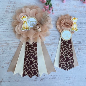 May include: Two brown and white giraffe print sashes with a flower and giraffe design. The sashes have the text "Mommy to Be" and "Daddy to Be" on them.