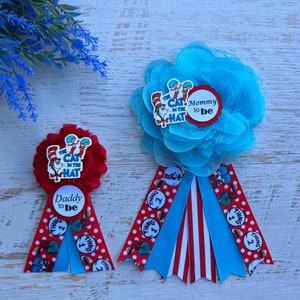 May include: Two red and blue 'Cat in the Hat' themed baby shower boutonnieres. One says 'Mommy to be' and the other says 'Daddy to be'.