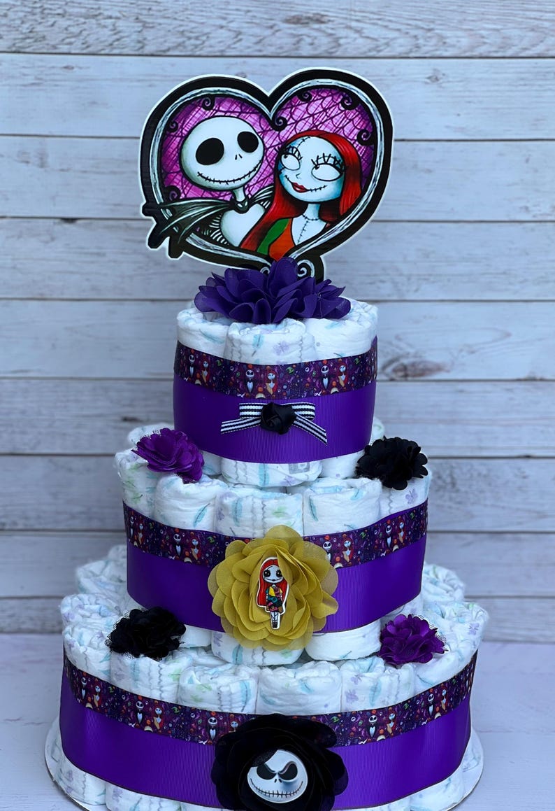 Puede incluir: Un pastel de pa&ntilde;ales de tres niveles decorado con cinta morada y negra, flores y un adorno con el tema de Jack y Sally. El pastel est&aacute; hecho de pa&ntilde;ales y es un regalo popular para baby shower.