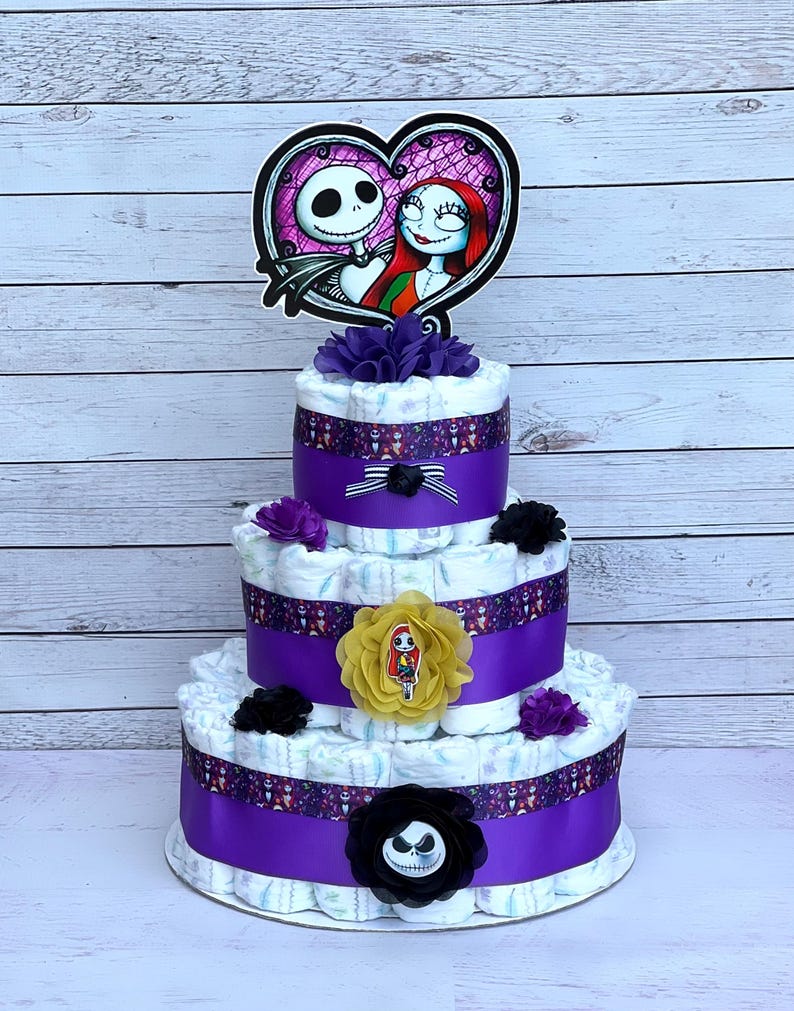 Puede incluir: Un pastel de pa&ntilde;ales de tres niveles decorado con cinta morada, flores negras y moradas, y una decoraci&oacute;n con el tema de Jack Skellington y Sally.