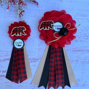 May include: Two red and black plaid sashes with bear and "Mommy to be" and "Daddy to be" text on the center circles. The sashes are decorated with black and tan ribbons.