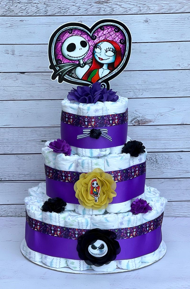 Puede incluir: Un pastel de pa&ntilde;ales de tres niveles decorado con cinta morada y negra, flores y una decoraci&oacute;n con el tema de Jack Skellington y Sally.