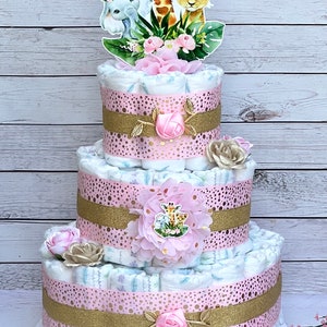 May include: A three-tier diaper cake decorated with pink and gold ribbon, pink flowers, and a topper featuring a giraffe, elephant, and lion.