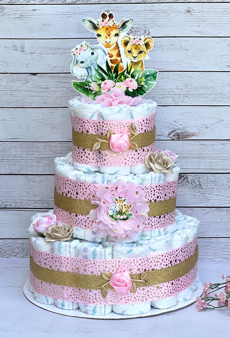 May include: A three-tier diaper cake decorated with pink and gold ribbon, pink flowers, and a topper featuring a giraffe, elephant, and lion.