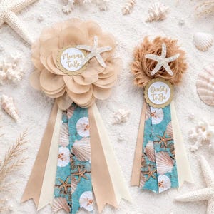 May include: Two decorative badges featuring beige fabric flowers, white glittery starfish accents, and ribbons with a teal and white seashell pattern. One badge displays the text Mommy To Be, and the other displays the text Daddy To Be in gold script.