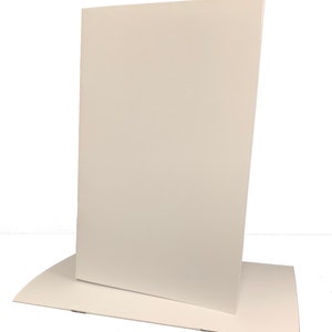 May include: A white cardboard display stand with a rectangular base and a tall, upright panel. The stand is designed to hold a sign or other printed material.