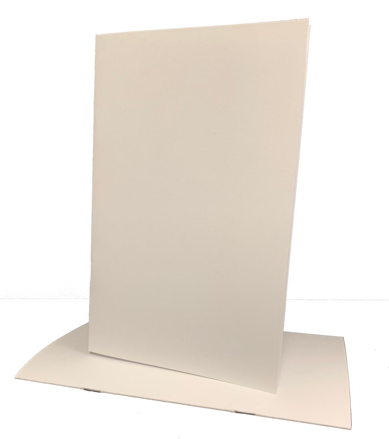 May include: A white cardboard display stand with a rectangular base and a tall, upright panel. The stand is designed to hold a sign or other printed material.