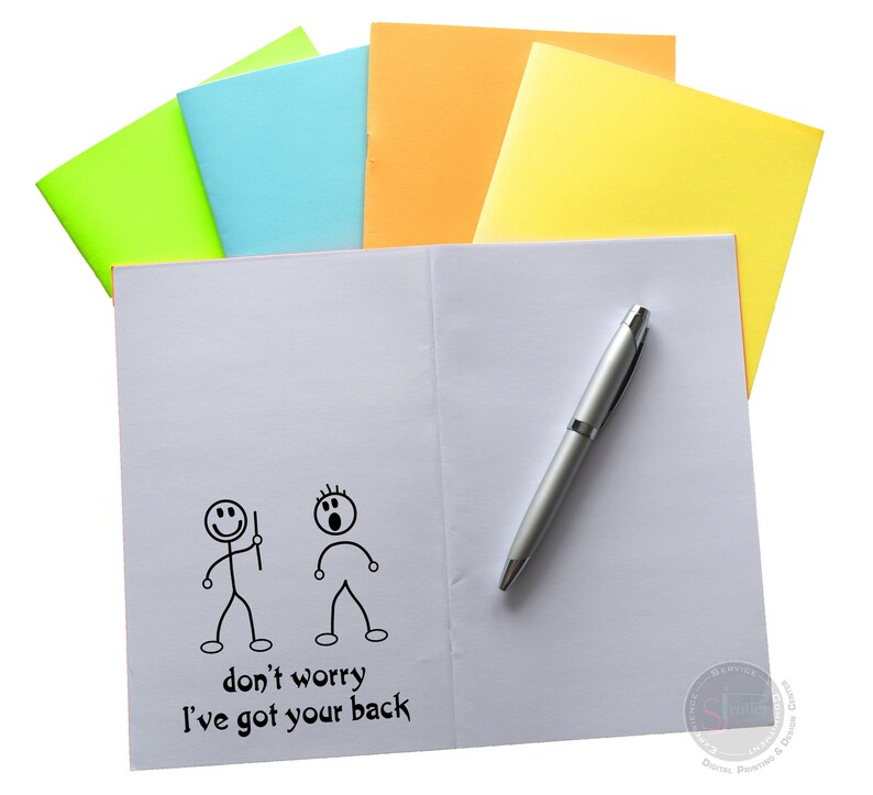 May include: A white notebook with a pen on top. The notebook has a drawing of two stick figures, one with a worried expression and the other with a confident expression. The text "don't worry I've got your back" is written below the figures.