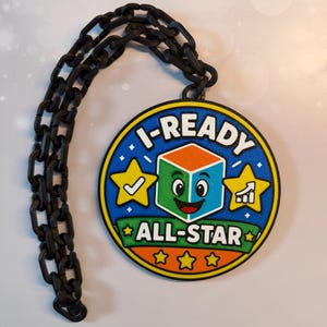 Puede incluir: Un medallón circular con un gráfico colorido de un personaje de cubo sonriente con el texto I-READY ALL-STAR. El diseño incluye estrellas amarillas con una marca de verificación y un icono de gráfico de crecimiento. Una cadena de plástico negro está unida.