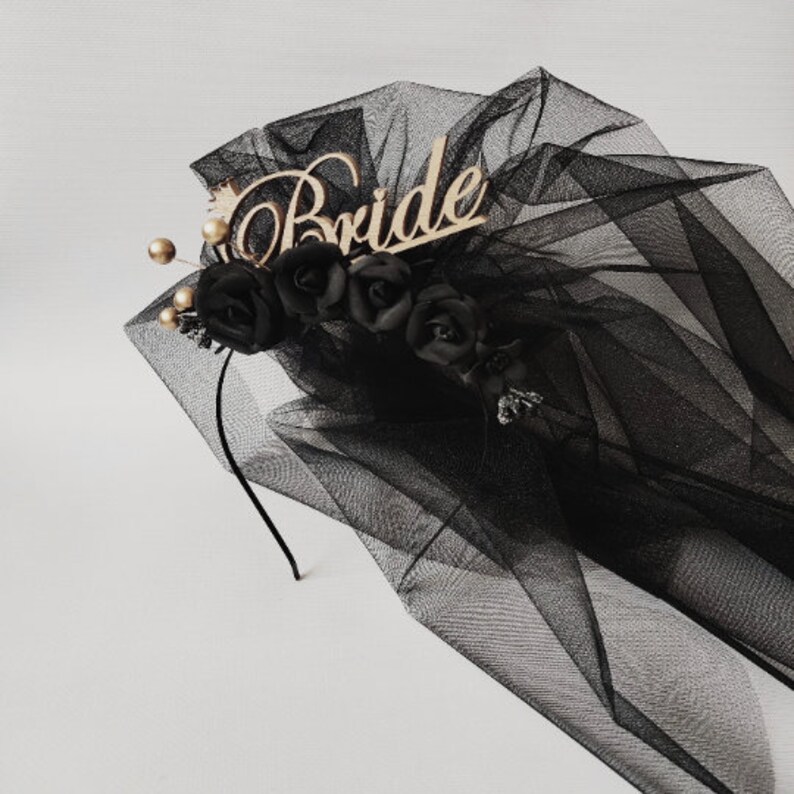 May include: Black bridal veil with a wooden "Bride" inscription. The veil is adorned with black roses and gold accents. The veil is made of a sheer, flowing fabric, perfect for a wedding or bachelorette party.
