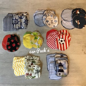 Könnte beinhalten: Ein Set mit 6 runden Stoff-Make-up-Entferner-Pads mit verschiedenen Mustern, darunter Zitronen, Erdbeeren, Anker und Streifen. Die Pads sind in Reihen auf einer Holzoberfläche angeordnet. Der Text "6er Pack's" ist in der Mitte des Bildes sichtbar.