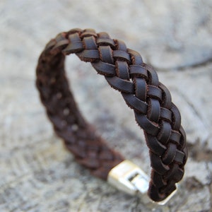 Può includere: Un braccialetto in pelle marrone con un design intrecciato e una chiusura argentata.