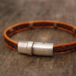 Puede incluir: Un brazalete de cuero marr&oacute;n con un cierre de plata. El brazalete est&aacute; trenzado con dos tonos diferentes de cuero marr&oacute;n.