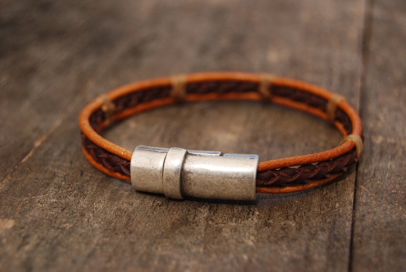 Puede incluir: Un brazalete de cuero marr&oacute;n con un cierre de plata. El brazalete est&aacute; trenzado con dos tonos diferentes de cuero marr&oacute;n.
