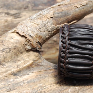 May include: A brown leather bracelet with a braided design. The bracelet is made of thick, supple leather and has a rustic look.