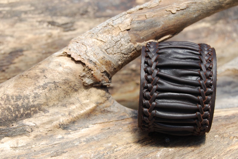 May include: A brown leather bracelet with a braided design. The bracelet is made of thick, supple leather and has a rustic look.