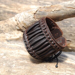 May include: A brown leather bracelet with a braided design and a black cord closure.