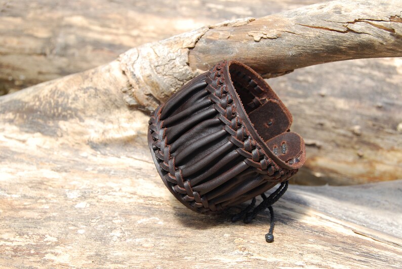 May include: A brown leather bracelet with a braided design and a black cord closure.