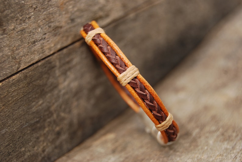 Puede incluir: Un brazalete de cuero trenzado con hebras de cuero marr&oacute;n y tostado. El brazalete est&aacute; tejido en un patr&oacute;n simple.