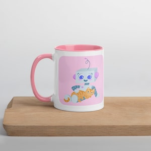Puede incluir: Taza de cerámica blanca con interior y asa rosas. La taza presenta una ilustración de dibujos animados de un robot abrazando a un gato atigrado naranja sobre un fondo rosa. La taza está sobre una superficie de madera.