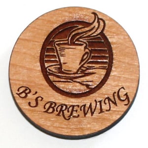 Puede incluir: Un posavasos redondo de madera con un dise&ntilde;o grabado en marr&oacute;n de una taza de caf&eacute; humeante. El texto "B'S BREWING" est&aacute; grabado debajo del dise&ntilde;o.