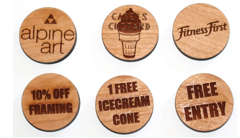 Puede incluir: Seis fichas redondas de madera con varios dise&ntilde;os y textos. Las fichas presentan logotipos para empresas como "Alpine Art", "Case's Custard" y "Fitness First". Otras fichas ofrecen descuentos como "10% de descuento en enmarcar" y "1 cono de helado gratis".